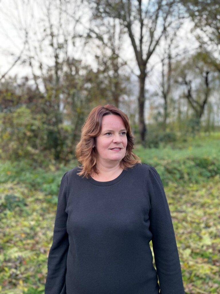 Petra van der Giessen buiten tussen het groen, ze kijkt opzij